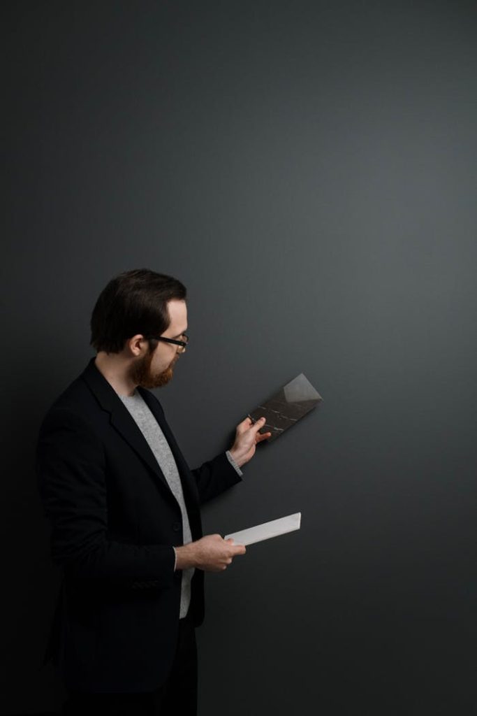 Man in a suit examining tile samples against a greenish wall, offering interior design insights.