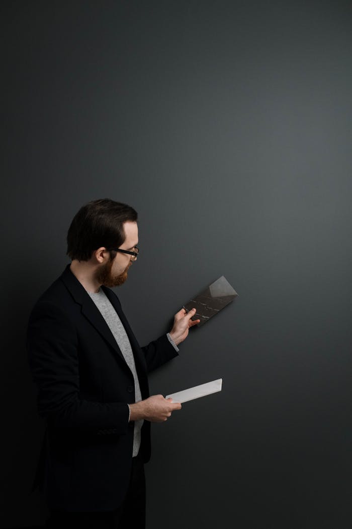 Man in a suit examining tile samples against a greenish wall, offering interior design insights.